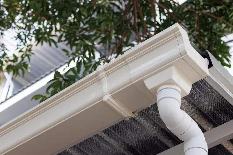Close-up of a cream-colored vinyl gutter and downspout in Smithtown, NY